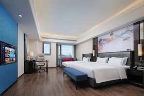 A modern hotel room with a large bed, a desk, and a view of the city.