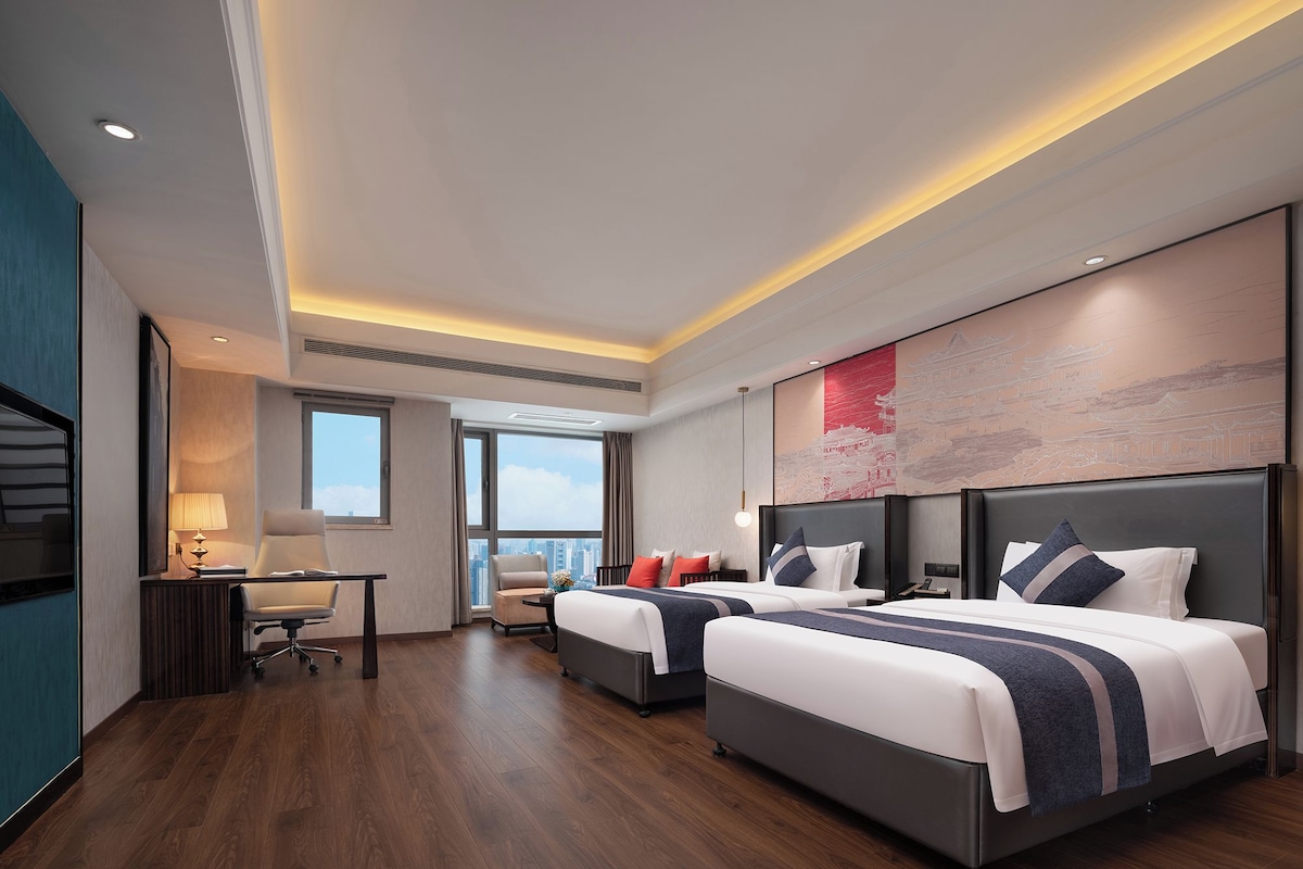 Una habitación de hotel moderna con dos camas, un escritorio y un ventanal grande.