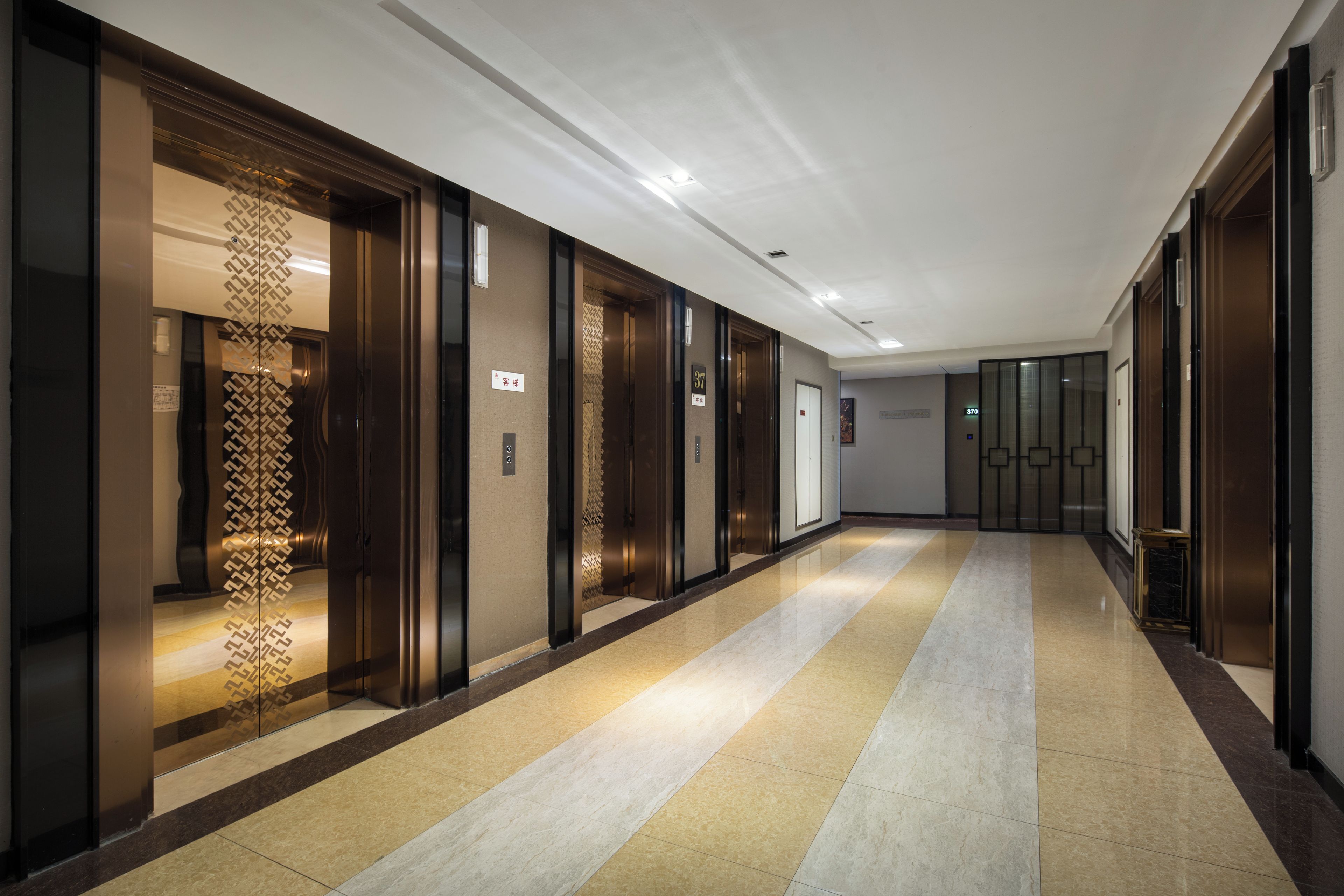 A hotel corridor with multiple elevators, a patterned glass wall, and a tiled floor.