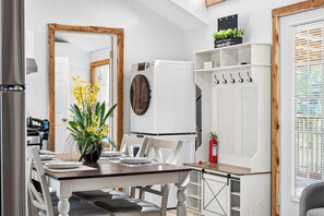 Un comedor con una mesa de madera dispuesta para cuatro, un armario blanco con ganchos y un electrodoméstico blanco al fondo.