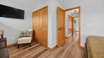 A bedroom with a wooden wardrobe, a bed, a chair, and a television on the wall.