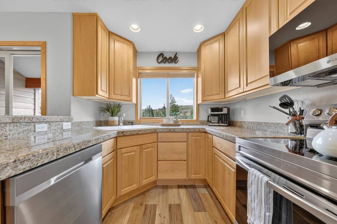 A modern kitchen with wooden cabinets, granite countertops, stainless steel appliances, and a window with a view.