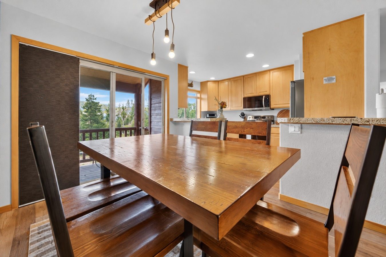 A modern kitchen with wooden cabinets, a large dining table, and a view to the outdoors.