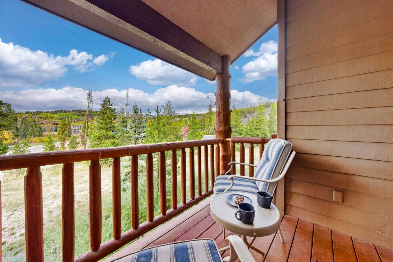 A wooden deck with a single chair and table, overlooking a forested area.