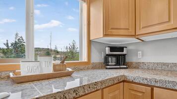 A kitchen with a coffee maker, a sign with 'SUGAR' and 'TEA,' and a view of trees and hills outside.