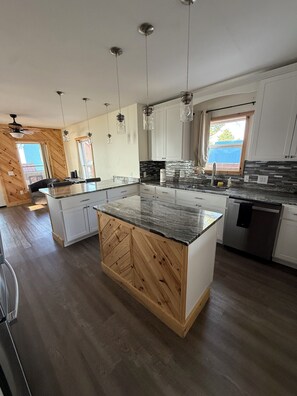 Cozinha moderna com ilha central, iluminação pendente e vista para o exterior.