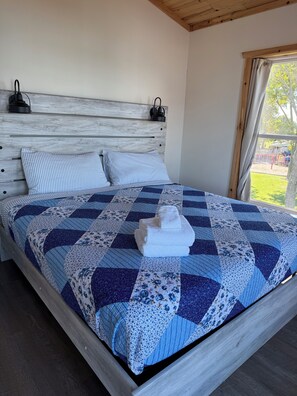 Un lit recouvert d’une couette bleue et blanche, deux oreillers à rayures et une serviette blanche pliée.