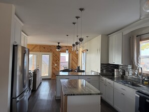A modern kitchen with a stainless steel refrigerator, wooden cabinets, a marble countertop, and pendant lighting. - 3-bedroom cabin centrally located between Geneva on the lake  & Ashtabula Harbor (Ashtabula)