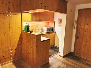 A compact kitchen with wooden cabinets, a microwave, a kettle, and a sink. - La Gemma by Interhome (Celerina)