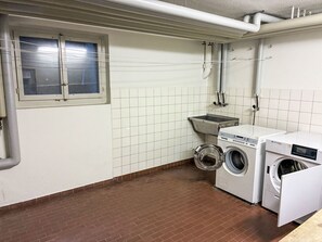 Ein Waschraum mit zwei Waschmaschinen, einem Wäscheständer und einem Fenster.