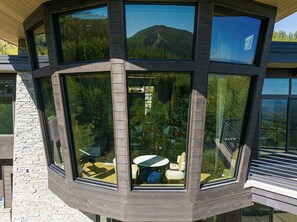 Ein Eckzimmer mit großen Fenstern und Blick auf einen bewaldeten Berg.