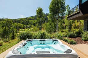 Een hottub met uitzicht op een bebost glooiend landschap en een gebouw op de achtergrond.