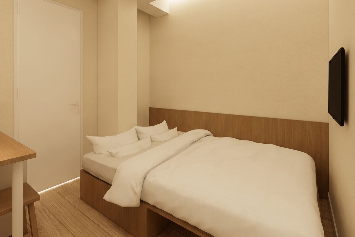 A minimalist hotel room with a bed, bedside table, and a wall-mounted TV.