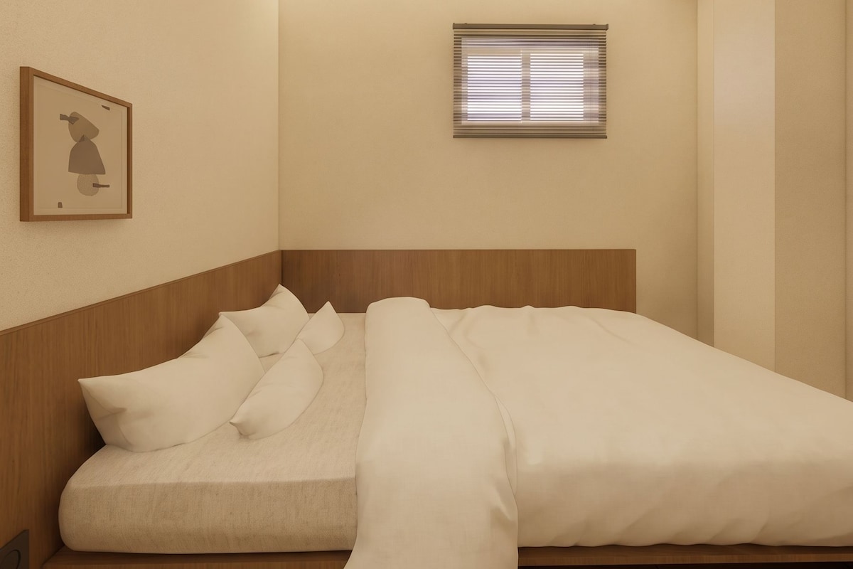 A compact bedroom with a bed, a small window with blinds, and a framed picture on the wall.
