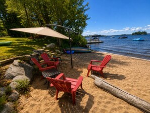 A beach setting with red Adirondack chairs, a table, and an umbrella. - The Lakefront Muskoka Detour (Gravenhurst)