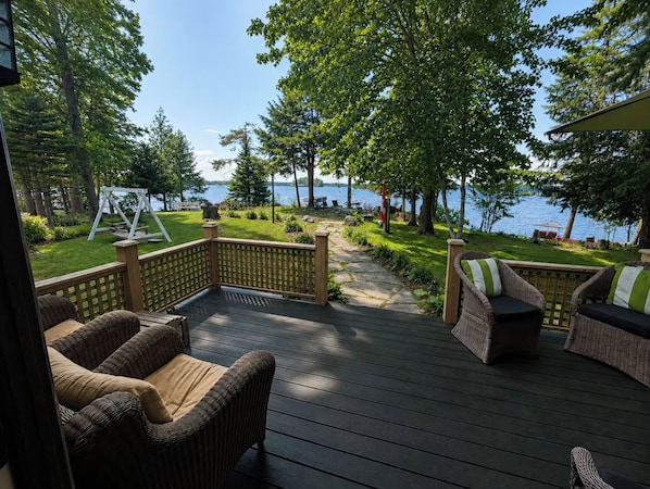 A wooden deck with wicker furniture, a pathway leading to a lake, and a swing set.