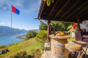 Un espacio al aire libre con vistas panorámicas a un lago y montañas, una bandera y un barril de madera.