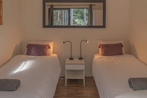 A twin room with two beds, a nightstand, a lamp, and a window with a view of greenery.