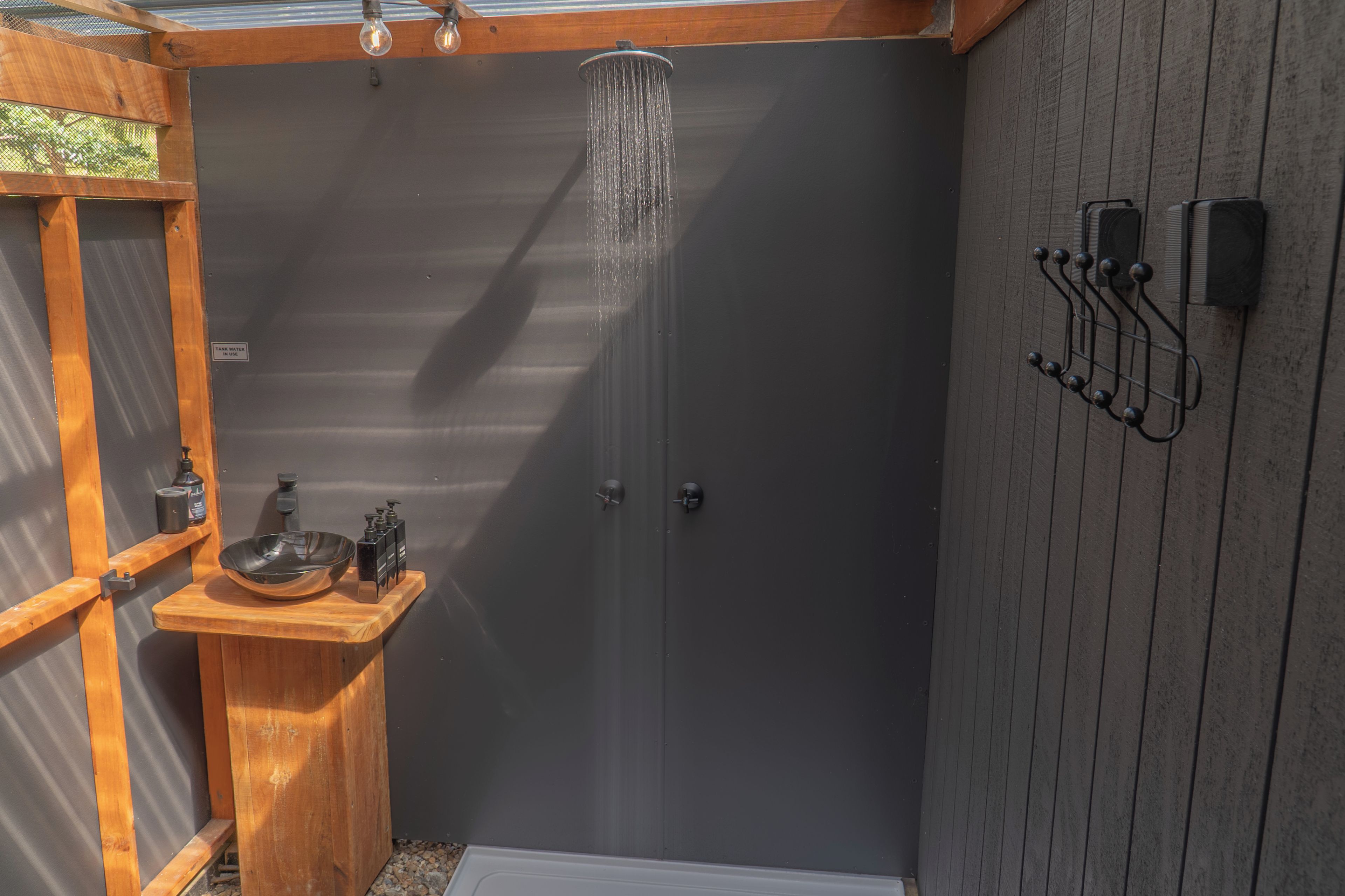 A shower enclosure with a wooden bench and a sink, a towel rack, and a showerhead.