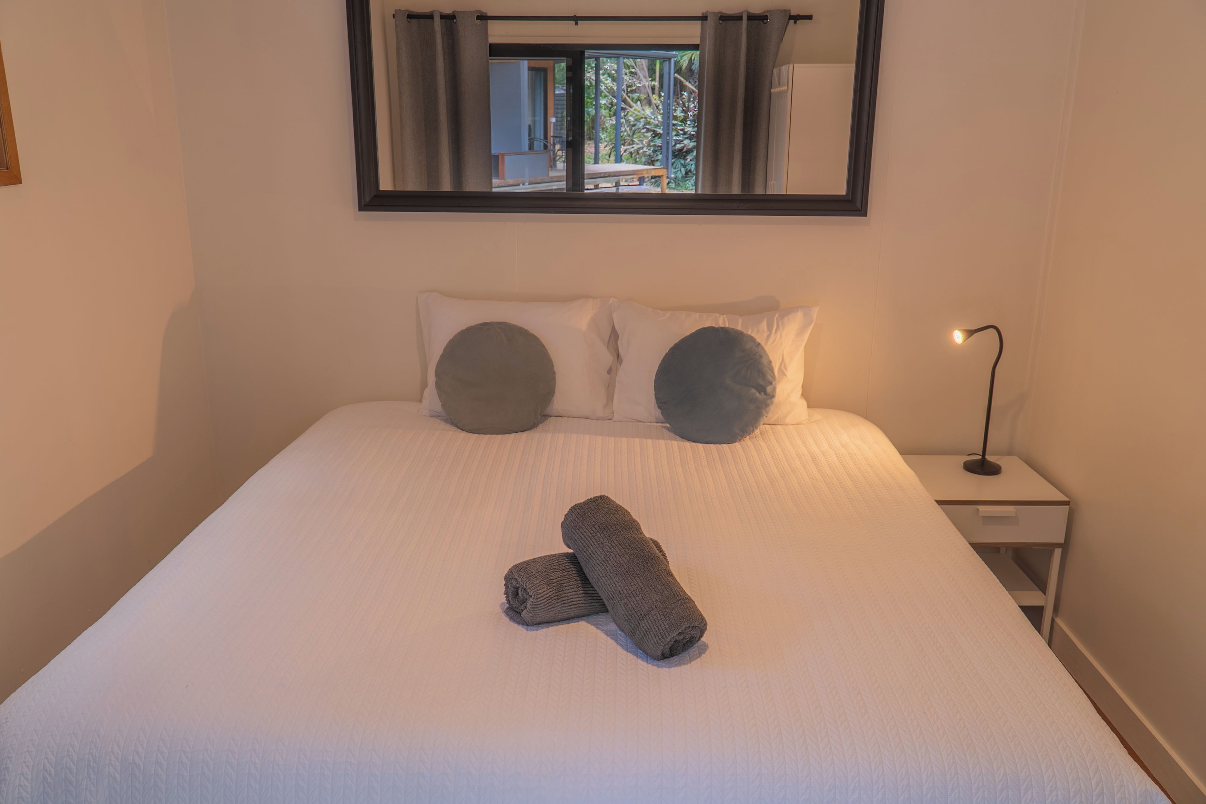 A neatly made bed with two pillows, a folded towel, and a bedside lamp.