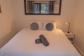 A neatly made bed with two pillows, a folded towel, and a bedside lamp.