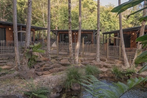 A natural setting with wooden cabins, a wooden fence, and a small stream.