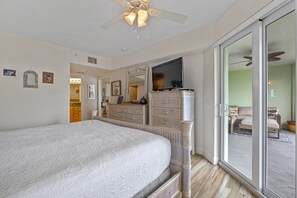 Ein Schlafzimmer mit einem großen Bett, einem Schminktisch, einem Fernseher und einer Glasschiebetür, die auf einen Balkon führt.