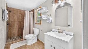A modern bathroom with a shower, toilet, sink, and a mirror. - Beautiful Cabin in Sparta w/King Bed (Sparta)