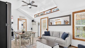 A modern kitchen with a built-in refrigerator, a dining area with a table and chairs, a gray sofa with blue cushions, and a ceiling fan. - Beautiful Cabin in Sparta w/King Bed (Sparta)