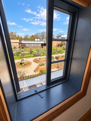 A window with a view of a garden, a metal roof, and a brick wall.