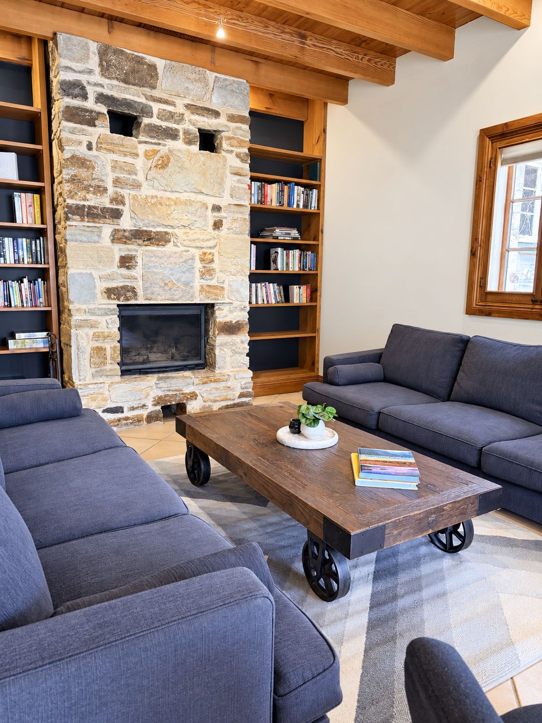 A living room with a stone fireplace, a sofa, a coffee table, and bookshelves.