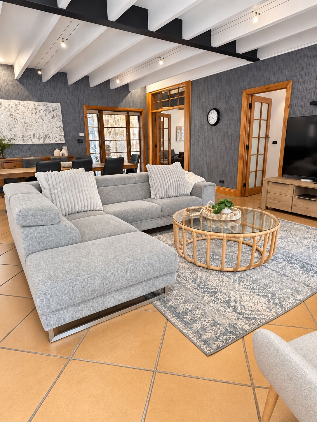 A modern living room with a sectional sofa, a glass coffee table, and a large flat-screen TV.