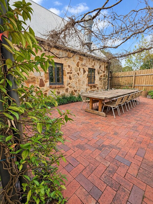 A stone building with a brick patio, a wooden table with chairs, and a view of the sky.