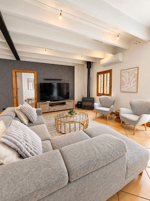 A modern living room with a sectional sofa, a flat-screen TV, a fireplace, and a large window.