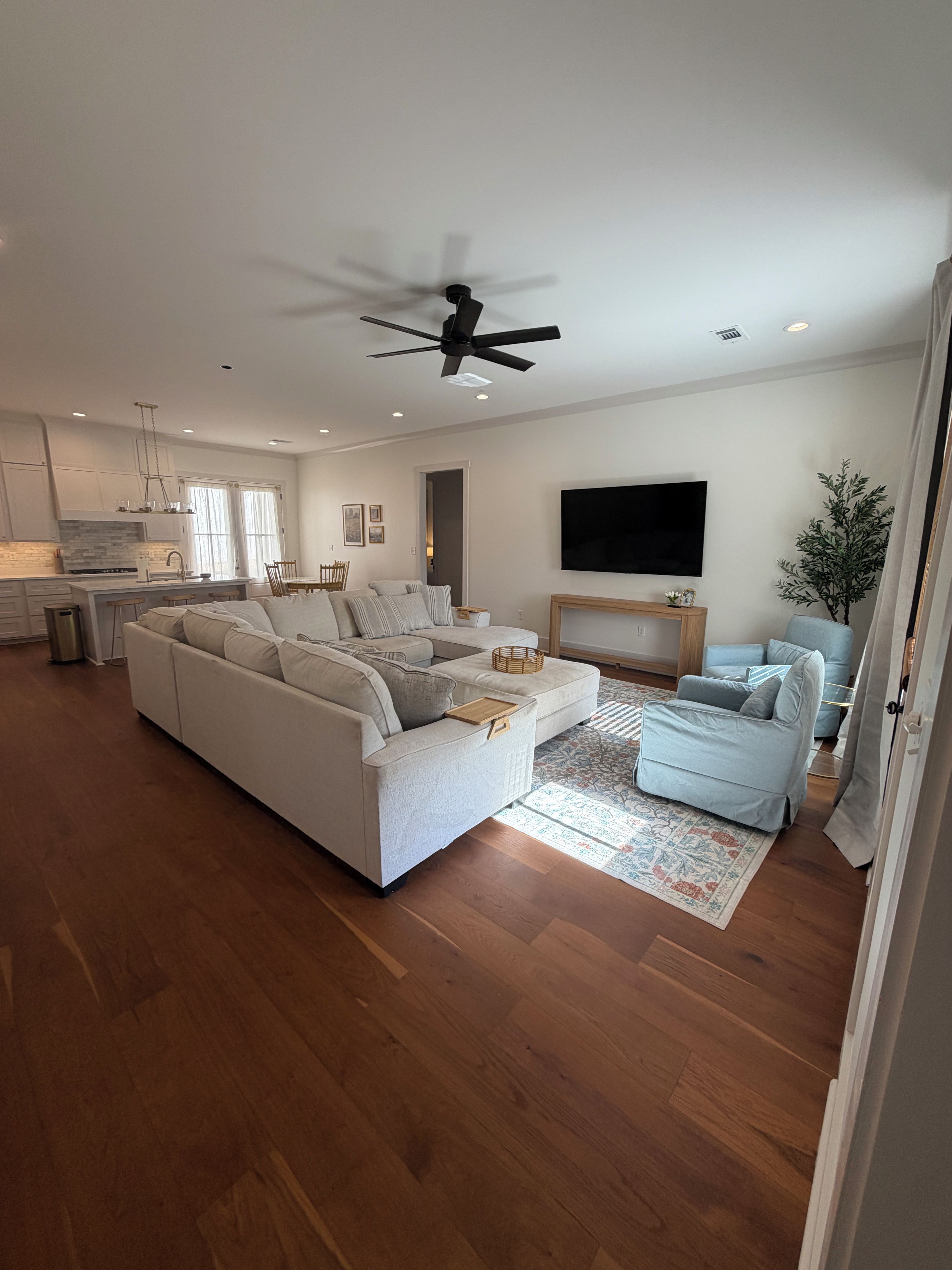 A modern living room with a sectional sofa, a TV, and a ceiling fan.