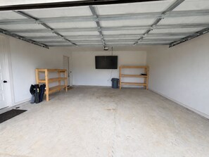 A garage with a concrete floor, two wooden shelves, a black trash bin, and a door.