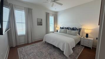 Une chambre à coucher avec un lit, des tables de chevet, un ventilateur de plafond et une fenêtre avec des rideaux.