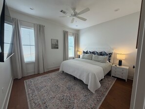 Une chambre à coucher avec un lit, des tables de chevet, un ventilateur de plafond et une fenêtre avec des rideaux.