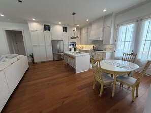 Une cuisine moderne avec des meubles blancs, un îlot central doté de tabourets et une table à manger avec des chaises.