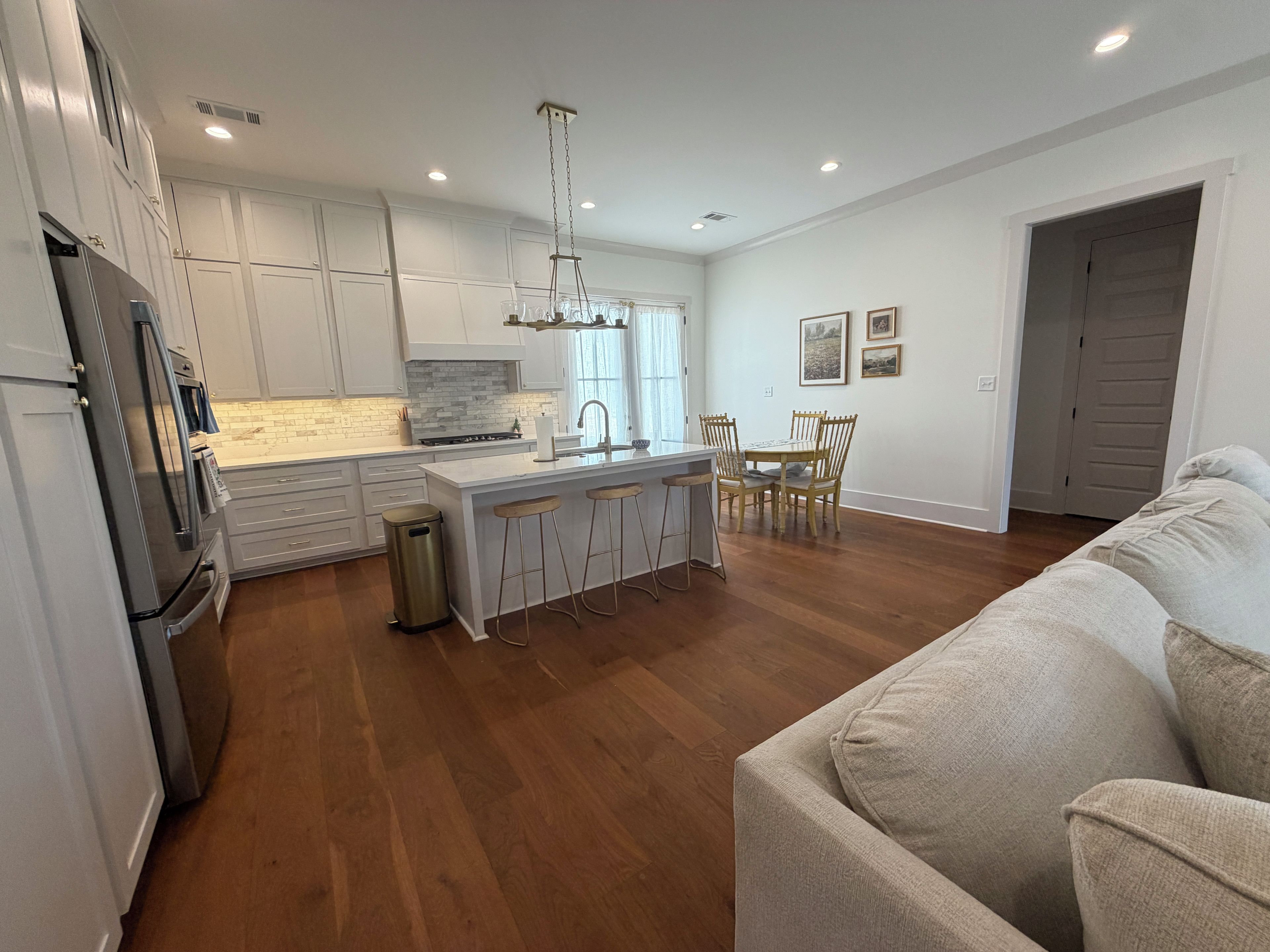 A modern kitchen with white cabinetry, a stainless steel refrigerator, and a wooden dining table with chairs.