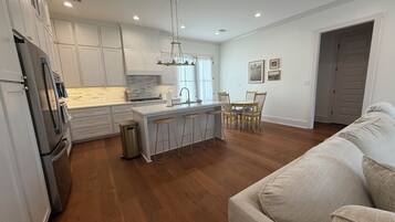A modern kitchen with white cabinetry, a stainless steel refrigerator, and a wooden dining table with chairs.