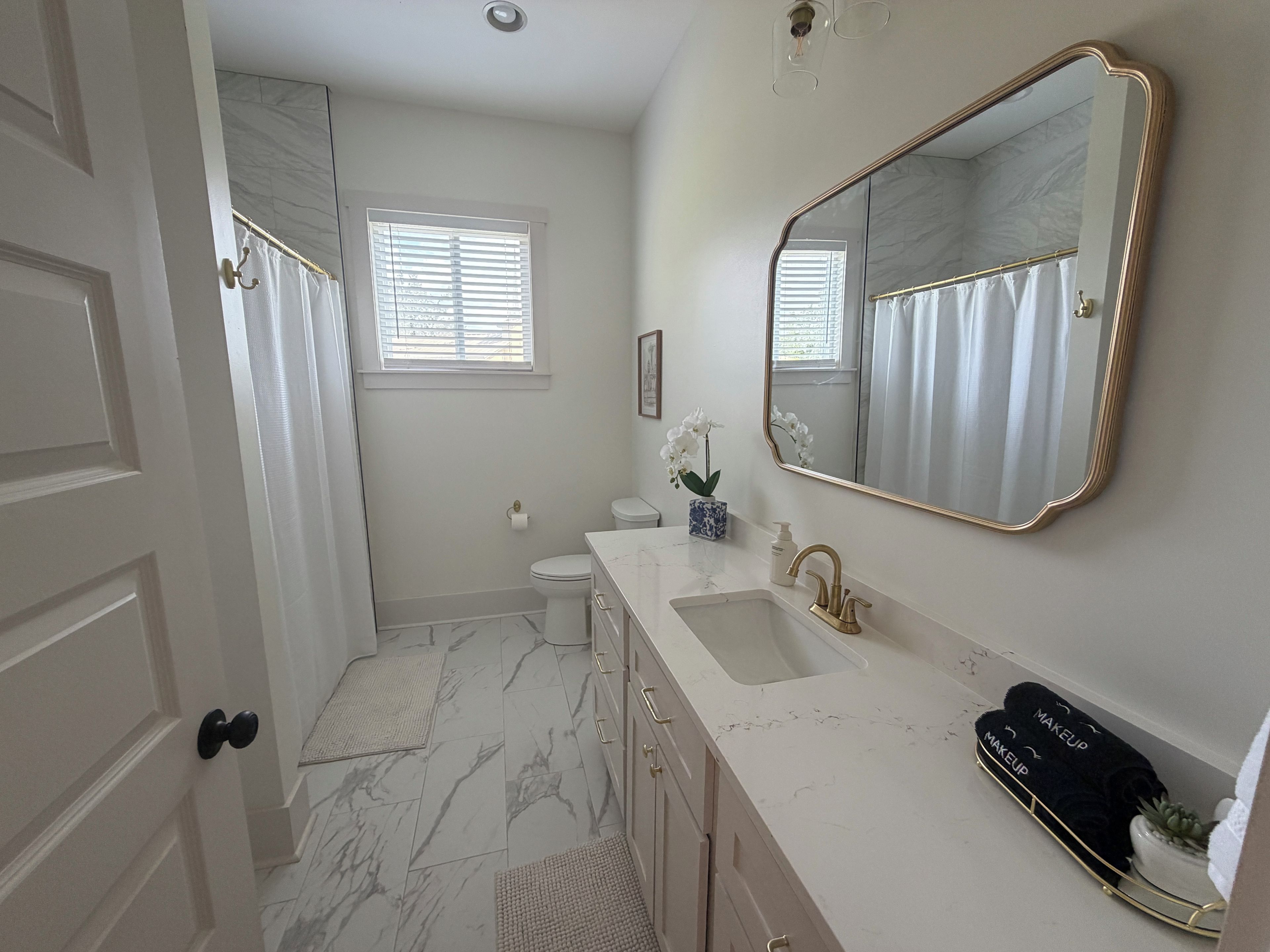 A bathroom with a marble floor, a white sink with gold fixtures, a large mirror, and a toilet.