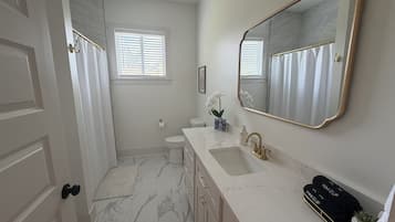 A bathroom with a marble floor, a white sink with gold fixtures, a large mirror, and a toilet.