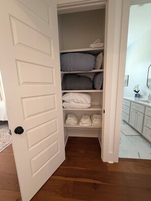 A walk-in closet with shelves for folded clothes, a mirror, and a small white vase with a flower.