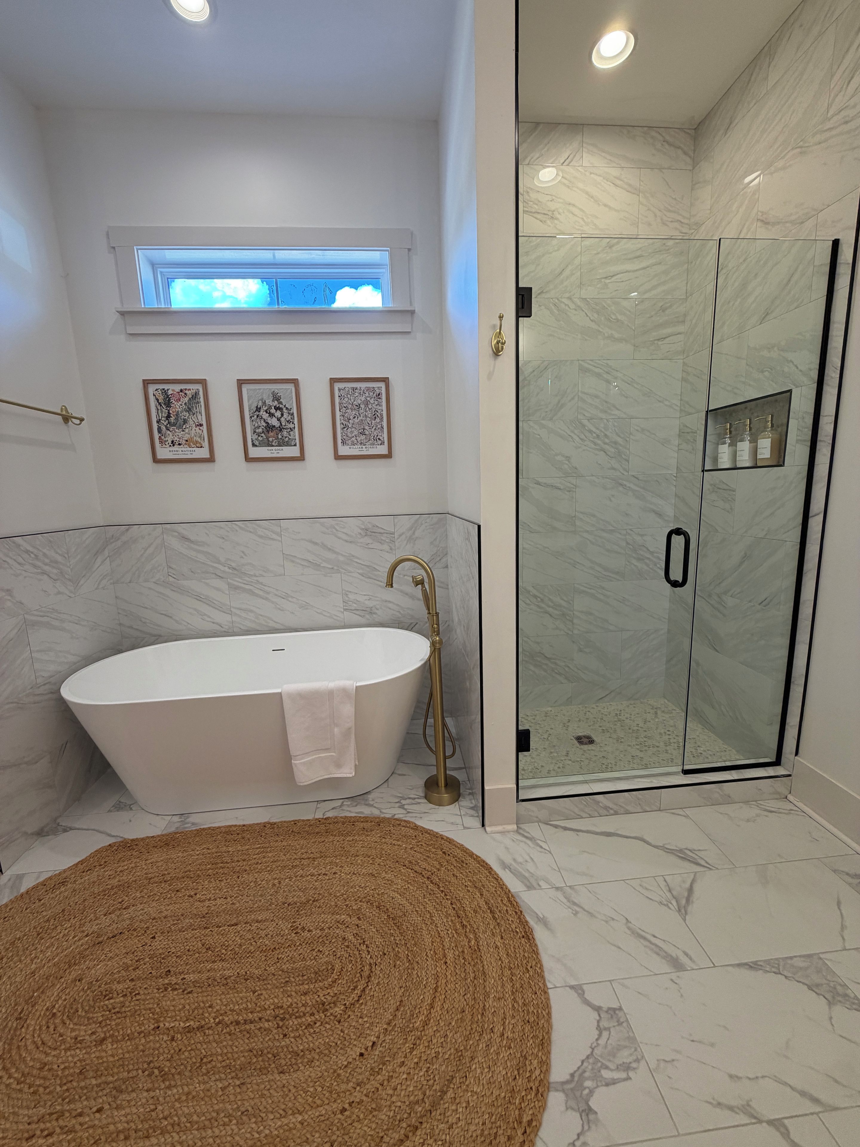 Un baño moderno con una bañera independiente, una cabina de ducha con mampara de vidrio y obras de arte enmarcadas en la pared.