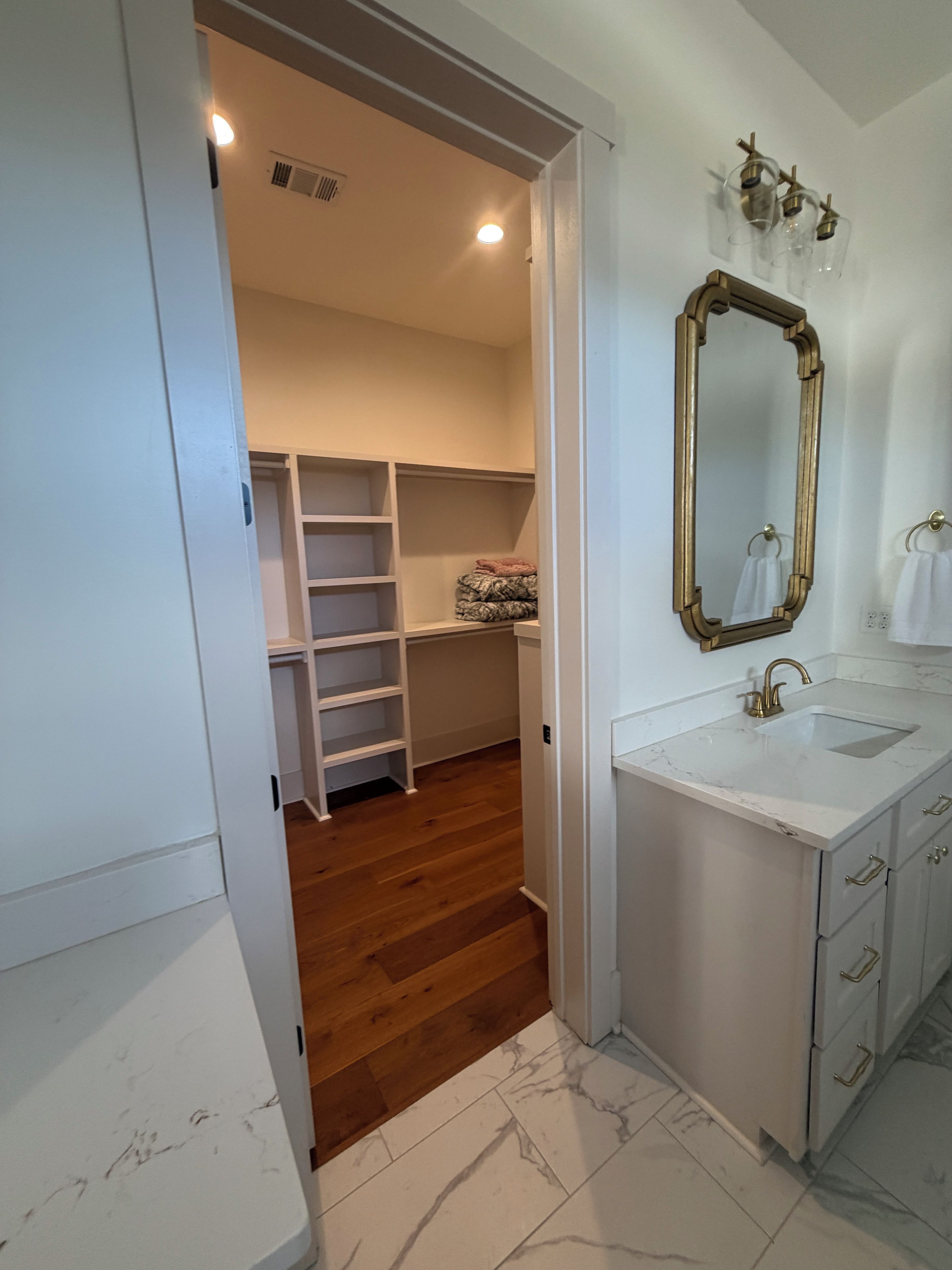 A bathroom with a white vanity, a mirror with a gold frame, and a wooden floor.