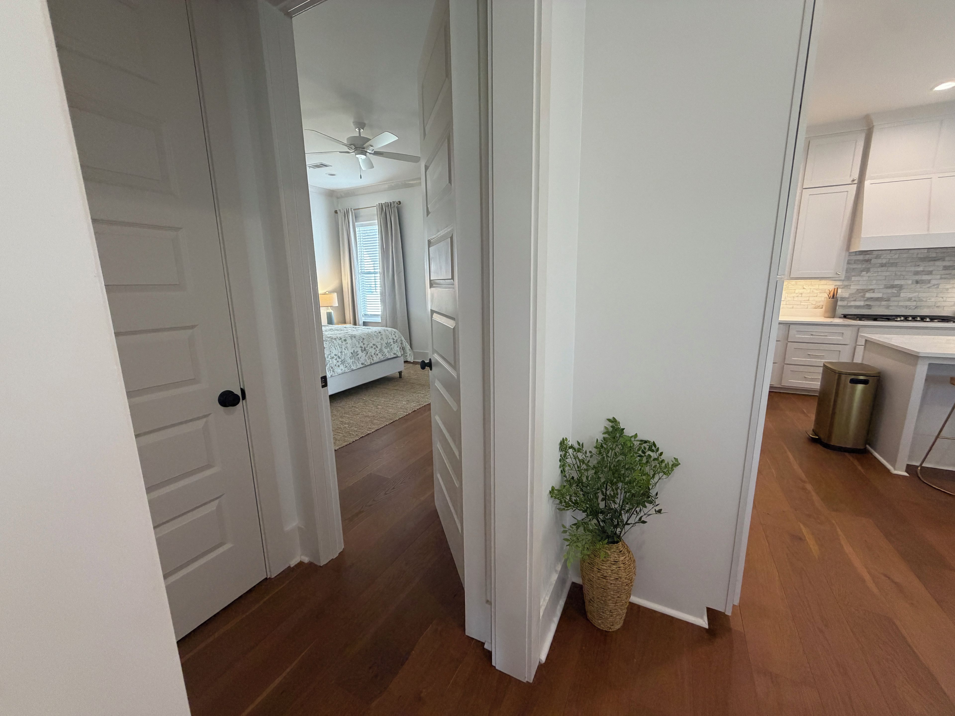 A hallway leading to a bedroom with a bed, a ceiling fan, and a plant.
