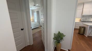 A hallway leading to a bedroom with a bed, a ceiling fan, and a plant.