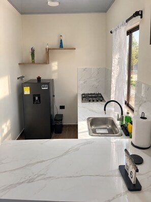 Pieni, käytännöllinen keittiö, jossa on jääkaappi, pesuallas ja liesi.