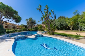 A swimming pool with a dolphin mosaic, surrounded by palm trees and a building in the background. - GuestReady - Marbella Park (Marbella)